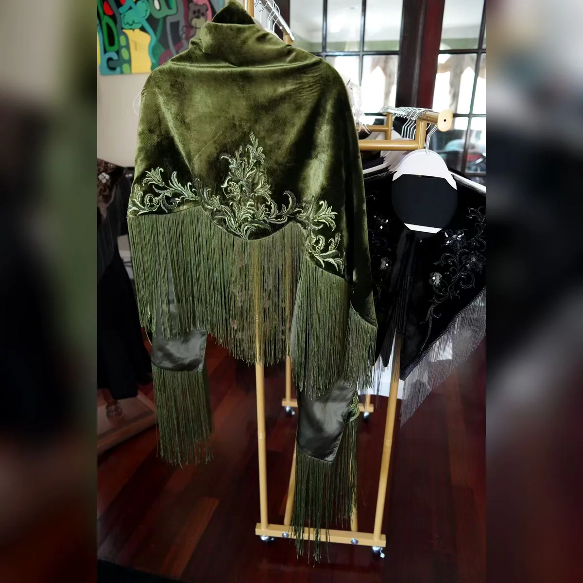 Olive velvet embroidered fringe shawl displayed on a garment rack
